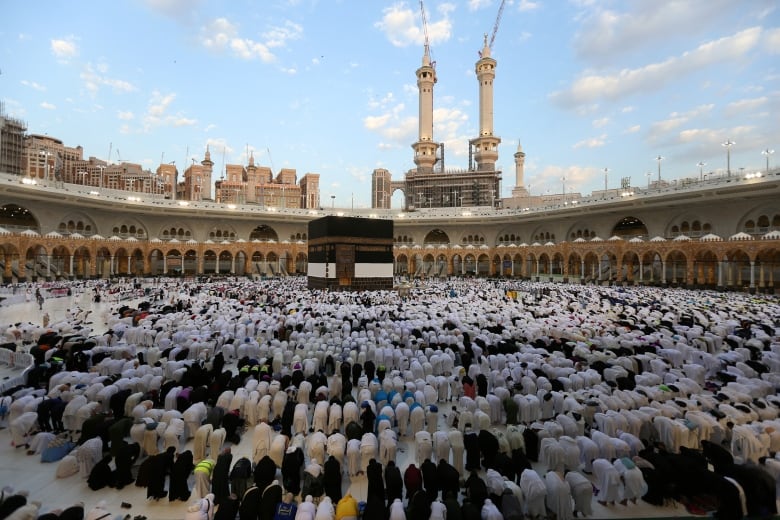 Muslim worshipers bow on their knees around the Kaaba, a square holy structure.