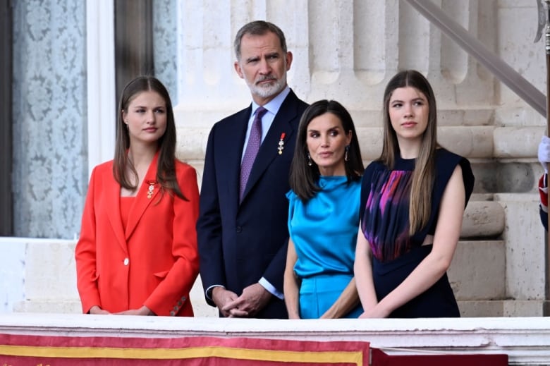 Four people stand on the balcony of a large stone building.