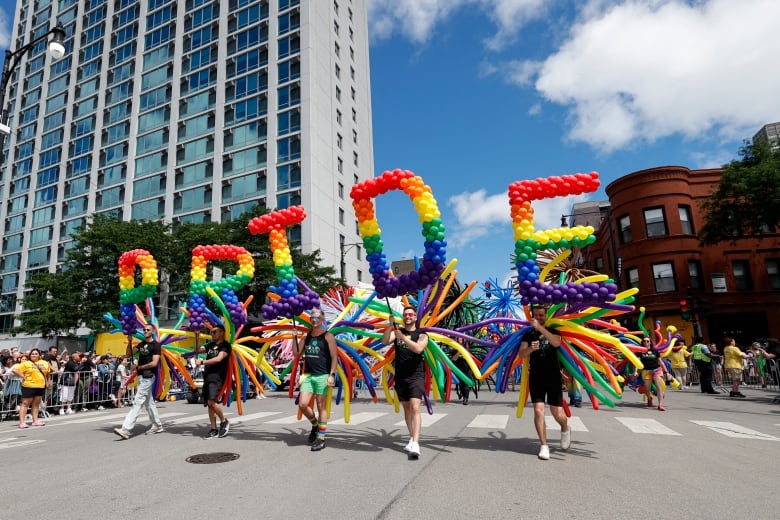 Marchers hold up balloons arranged to spell out, 'Pride.'
