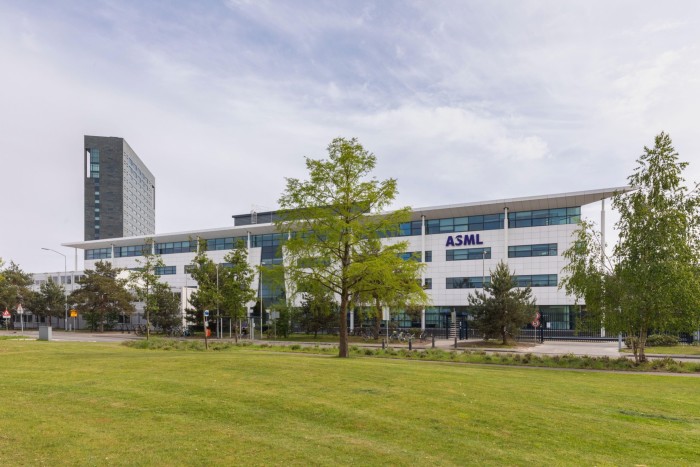 A modern office building with the logo “ASML” on the facade, set against a partly cloudy sky. The building is surrounded by trees and a well-maintained green lawn