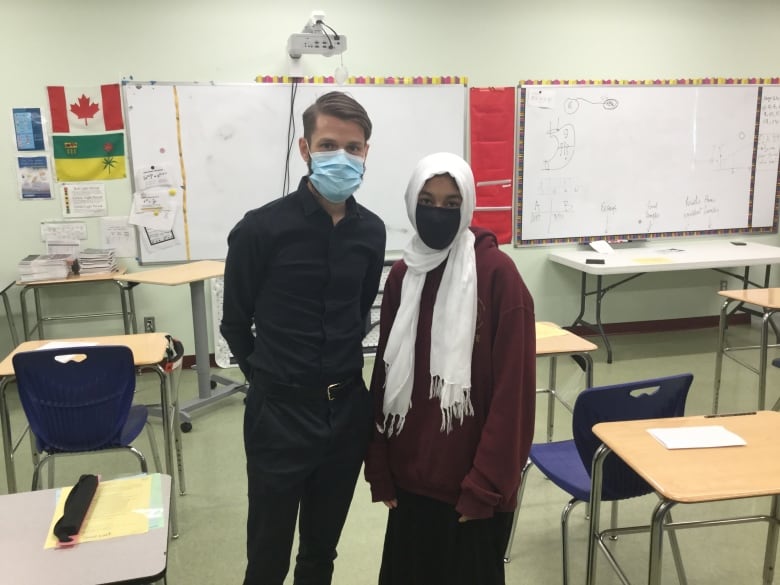 A masked man and a masked high school student stand amidst an empty classroom.