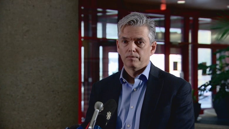 Edmonton Public Schools superintendent Darrel Robertson stands in front of a microphone by the front windows in the Centre for Education. Robertson has grey hair, and is wearing a blue shirt and dark suit jacket.