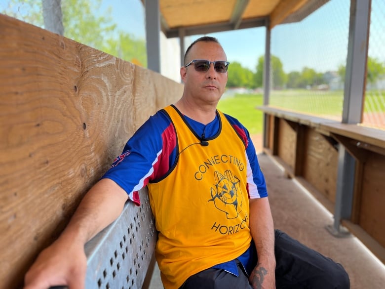 A man with a yellow jersey sits in a dugout of a baseball field.