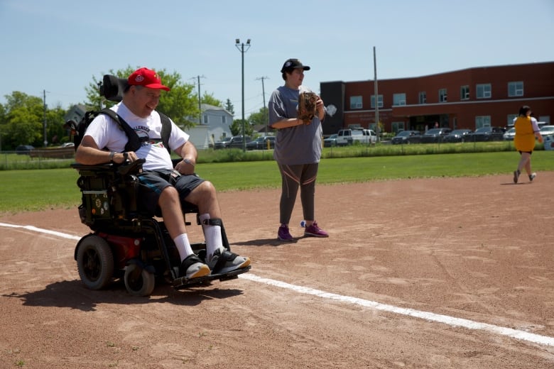 Michael Dell, in a wheel chair, stands at third base in a baseball field.