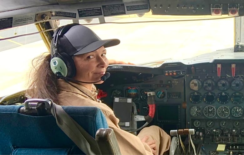 A pilot behind the controls of a plane. She is smiling and has long brown hair. 