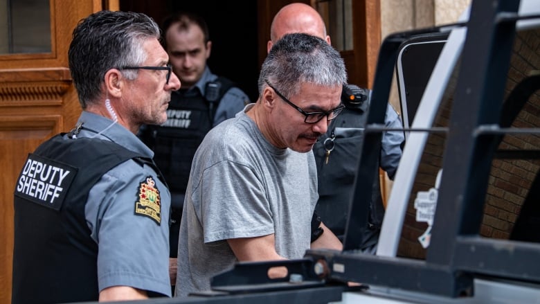 Man in handcuffs exits a court house and gets into vehicle with police escort.