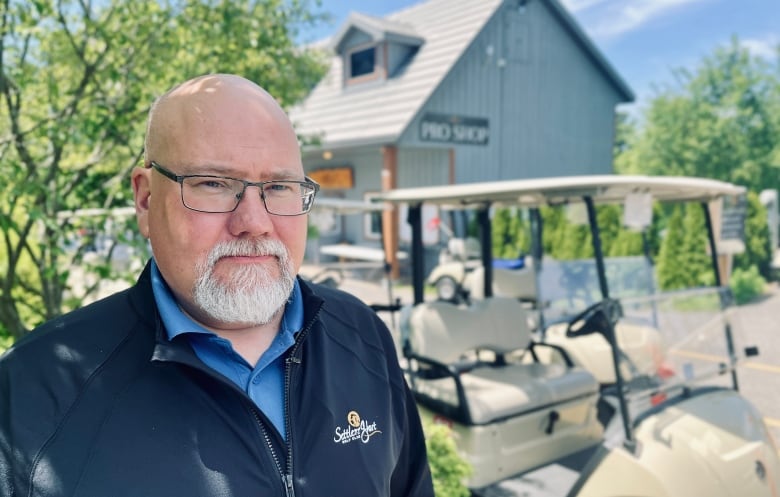 A man with glasses stands in front of golf carts at a golf course near Barrie, Ontario.