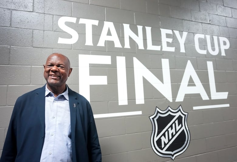 A smiling man in a blue jacket stands beside a wall painted with the words "Stanley Cup Final".