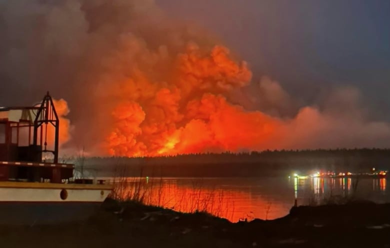 Smoke billows from a massive, angry red fire on the other side of a lake.