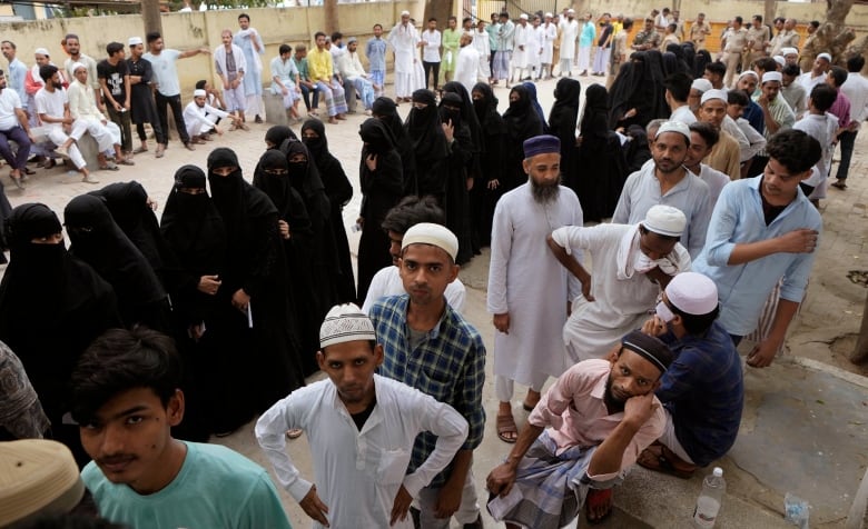 Women wearing long black robes and veils, and men stand in line to vote.