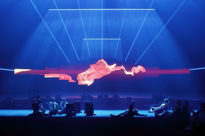 Stringly flames unfold on a long narrow video screen as blue lasers shoot out above