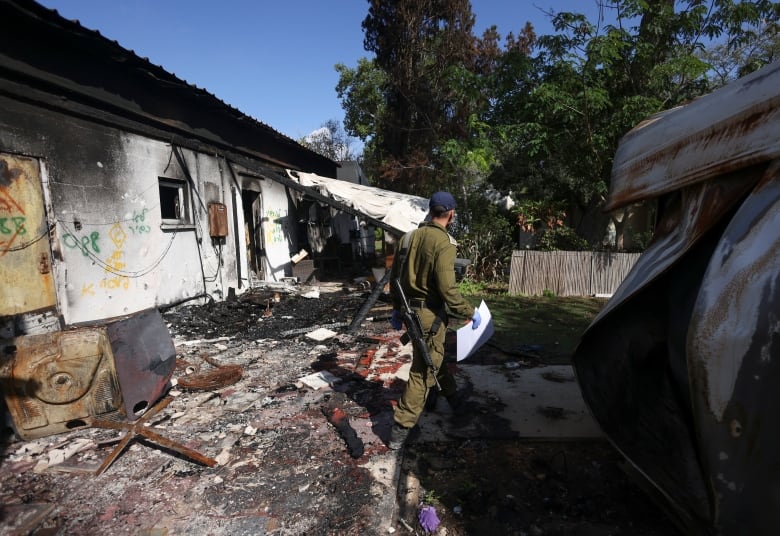 A soldier walks among the debris of a burnt house.