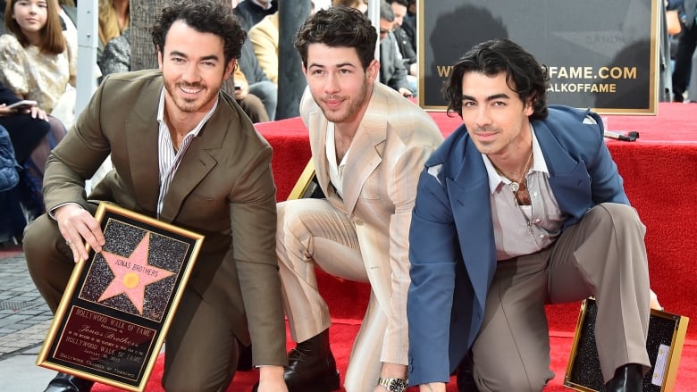 Three men in suits touch their hands to a Hollywood Star on the ground. 