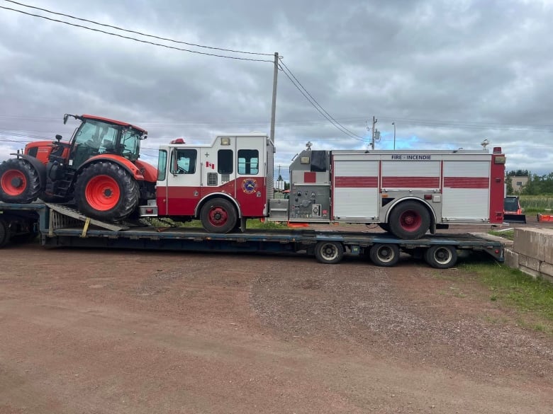 A fire truck loaded onto a flatbed truck for transport along with another piece of heeavy equipment.
