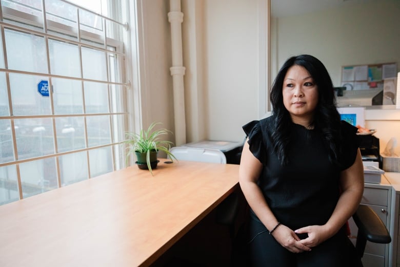 A woman in a black shirt looks out a window while sitting at a desk