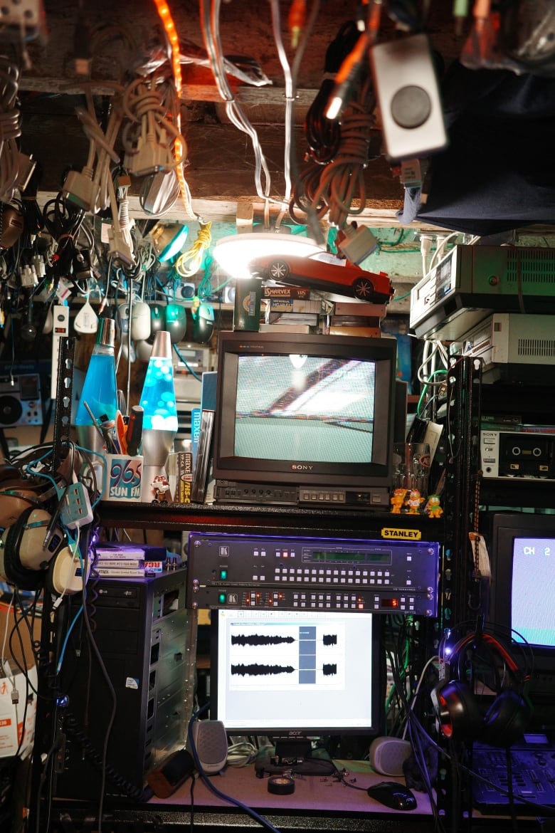 An editing station. A CRT television can be seen above a circuit board and an LCD computer monitor. Two lava lamps are next to the television, while various cords hang from the ceiling.