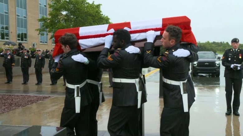 Military members carrying a casket draped with a Canadian flag. 