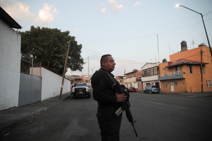 The officer stands in the middle of the street with his rifle pointing downwards