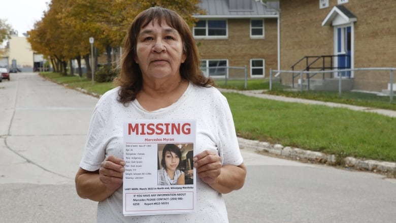 A woman holds up a missing persons poster for a younger woman.