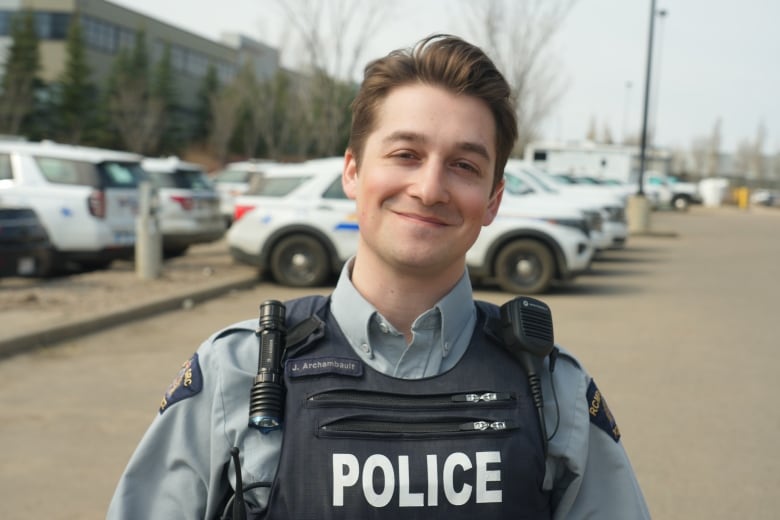 A policeman stands in front of police vehicles in the RCMP parking lot. 