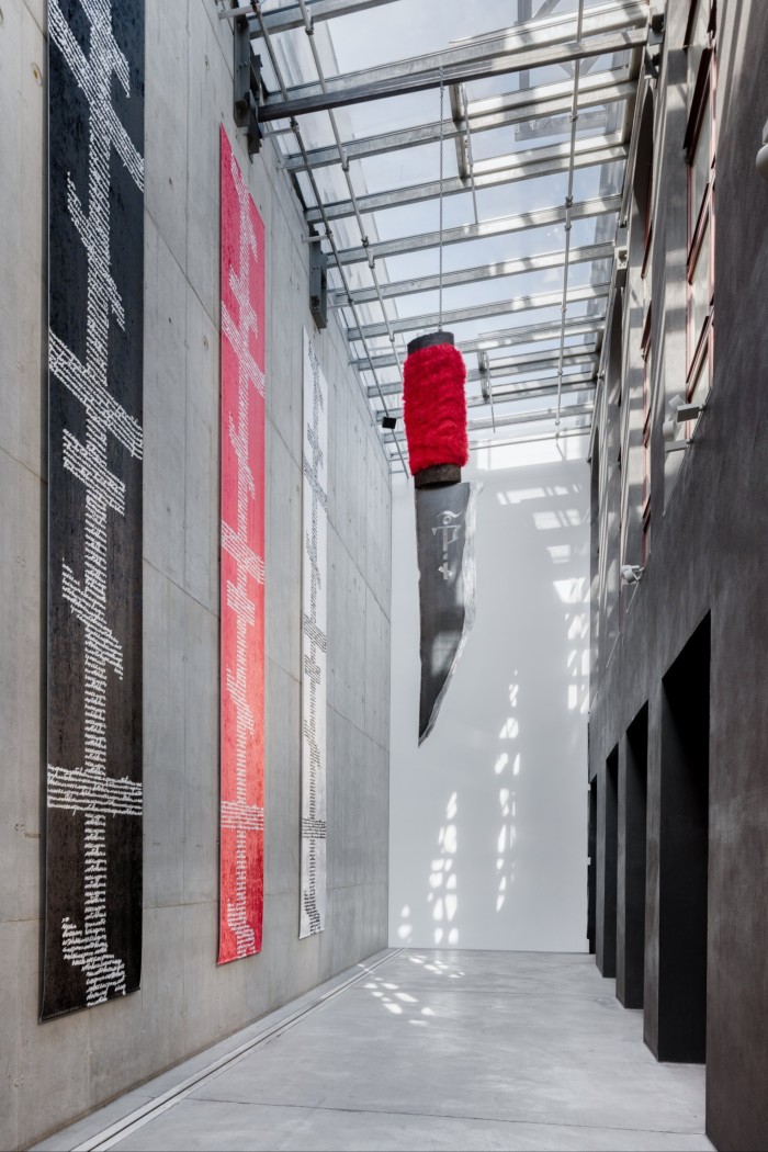 An art installation of a giant blade with a furry red handle hanging from the ceiling of a gallery space