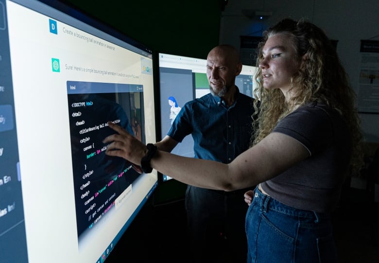 A man and woman stand in front of a large computer screen in a darkened room.