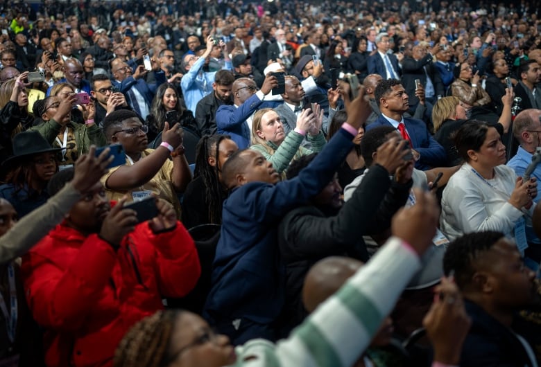 A crowd of people hold up their phones.