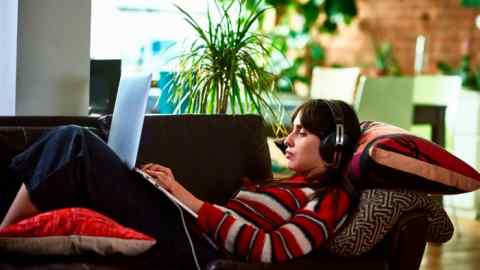 A woman working on her laptop and wearing headphones