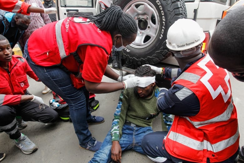 Medics in red vests tend to a man sitting on the street, his body slumped and his head wrapped in a bandage.