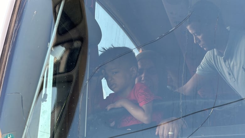 A young boy in a red T-shirt sits on his grandmother's lap inside a passenger bus.