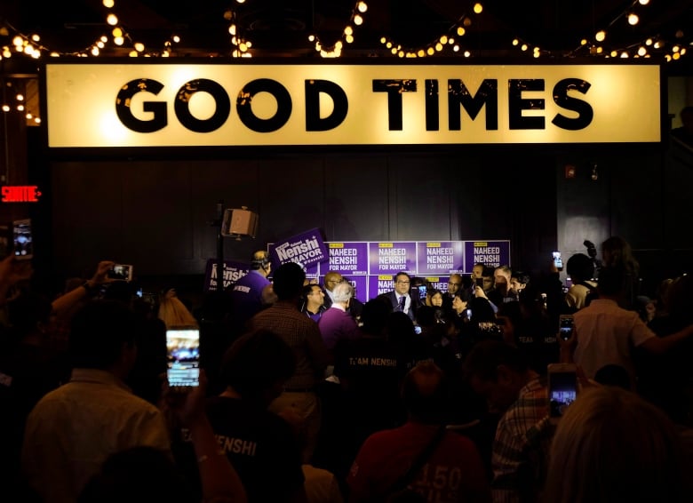 A "GOOD TIMES" sign in the foreground of an election night celebration for Nenshi.