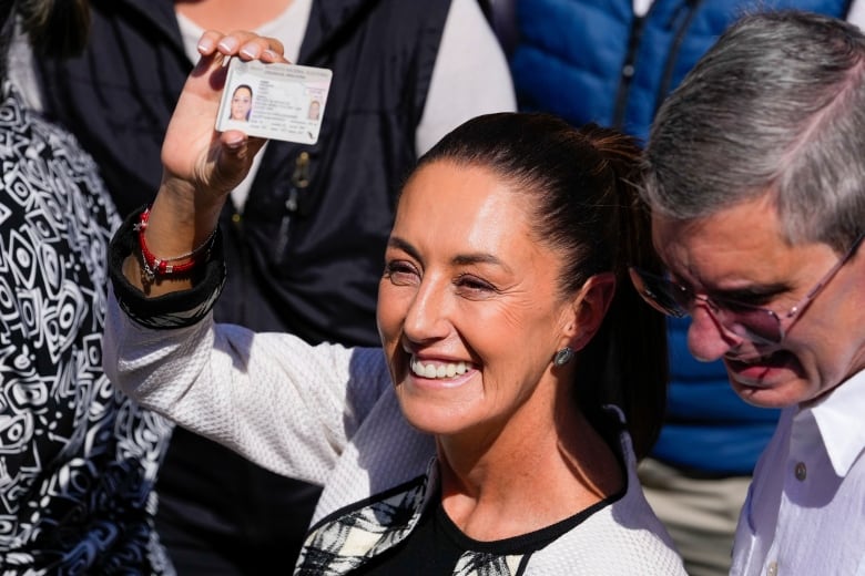 A woman smiles and holds up identification outside a polling centre.