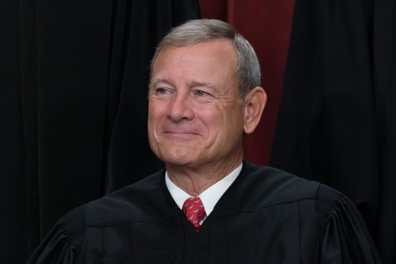 A clean-shaven man is shown in closeup wearing a judicial robe over a collared shirt and tie.