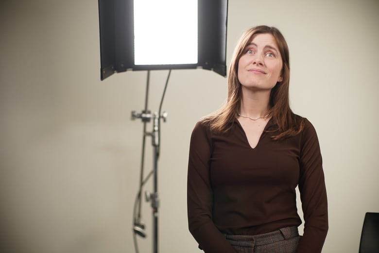 A woman wearing a brown shirt stands next to a light.