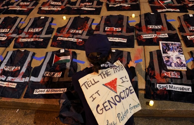 A  person kneels in front of a display  of vests