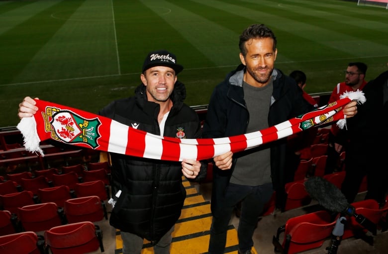 Two men hold a soccer team's branded scarf.