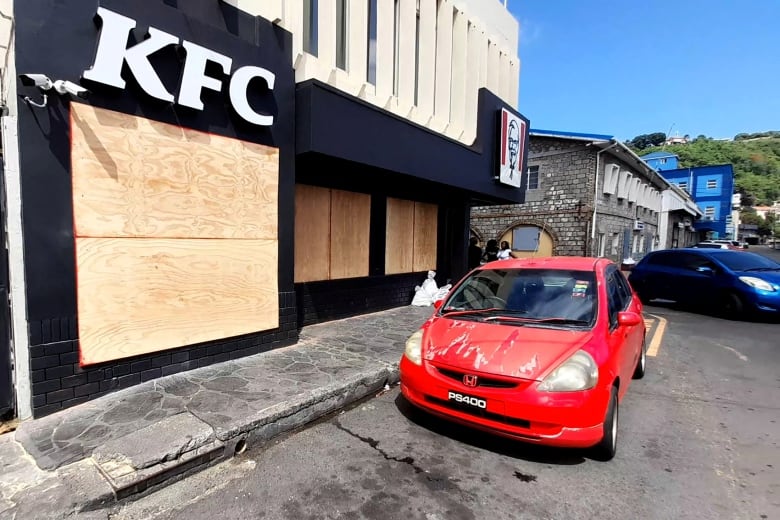 A small car outside a boarded-up building with the letters "KFC" on it.