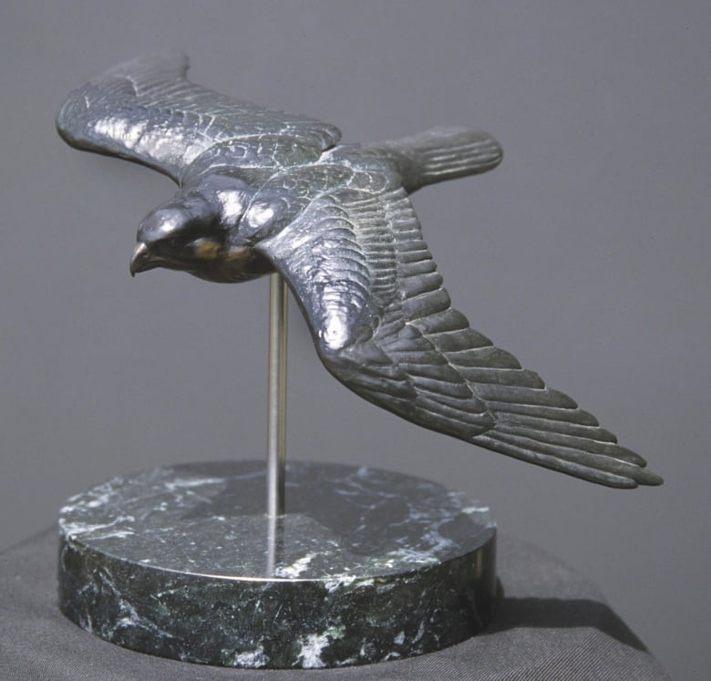 A small silver sculpture in bronze of a peregrine falcon on a pedestal.