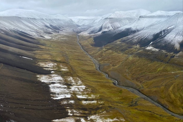 An aerial view captured from a helicopter shows snowy moutains and a river on the archipelago