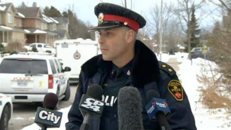 A police officer talks in front of microphones during a news scrum at a residential street.