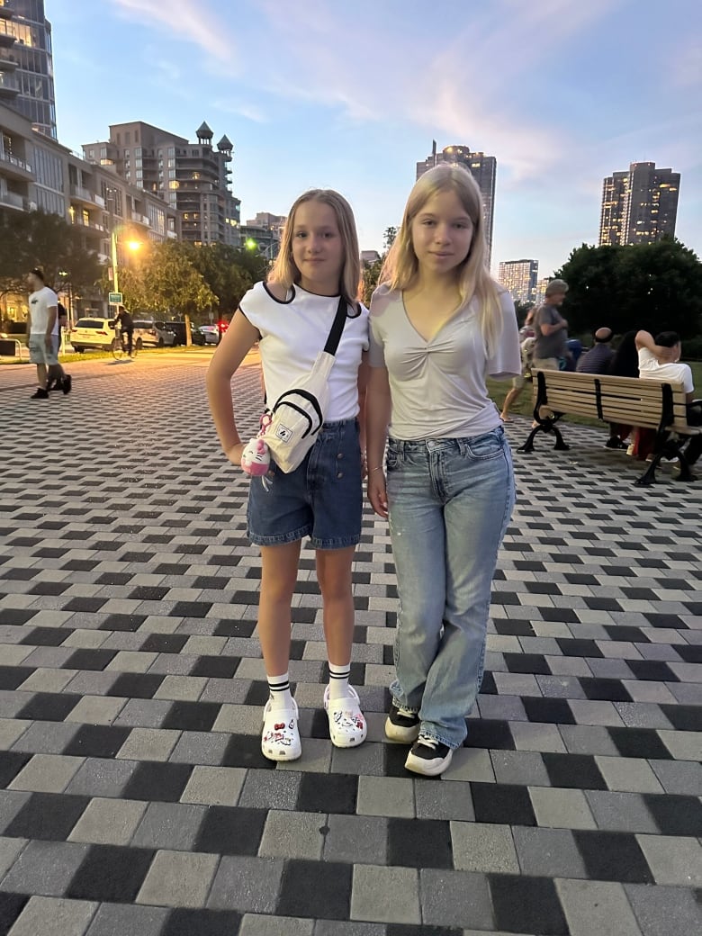 Two girls pose, one with her arm around the other. One girl has an amputated arm.