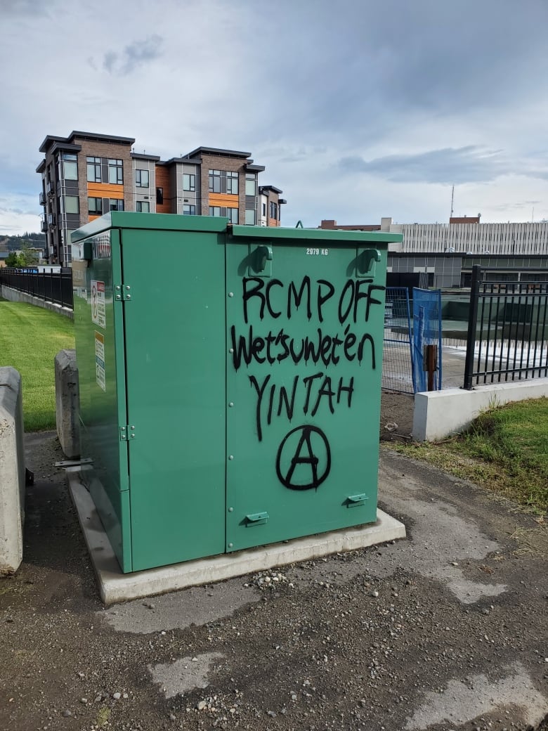 Black spray paint reads "RCMP off Wet'suwet'en Yintah" on a green electrical box. 