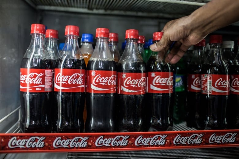 The hand of a man is shown reaching out to grab a bottle of coke from a display