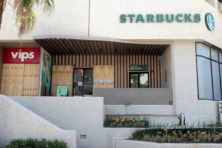 The front doors of two stores are covered in plywood.