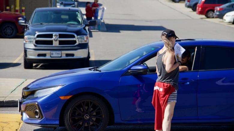 A person hands a driver a flyer through their open window.