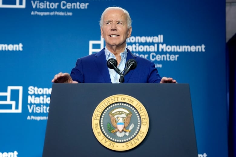 Joe Biden, wearing a navy blue suit, stands behind a blue podium bearing the presidential seal. There is a blue backdrop behind  him with the words "Stonewall National Monument Visitor Center" in white fonts. 