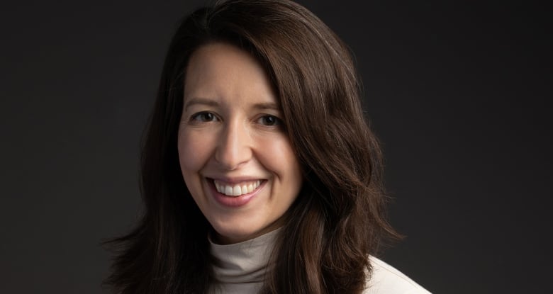 A portrait of a woman wearing a cream-coloured turtleneck shirt, with long, dark draped over her shoulders.