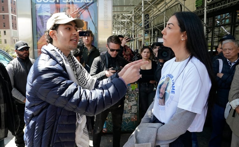 Two people have a heated discussion on the street while surrounded by a crowd.