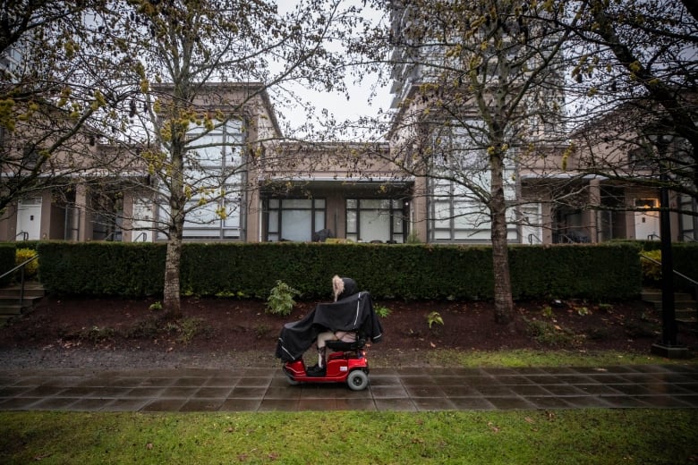 A person in a motorized scooter on a sidewalk in front of an apartment building