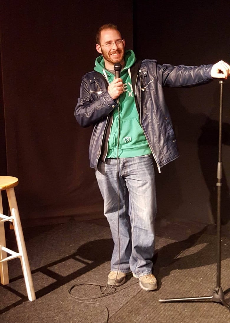 A smiling man in a leather jacket holds a microphone. 